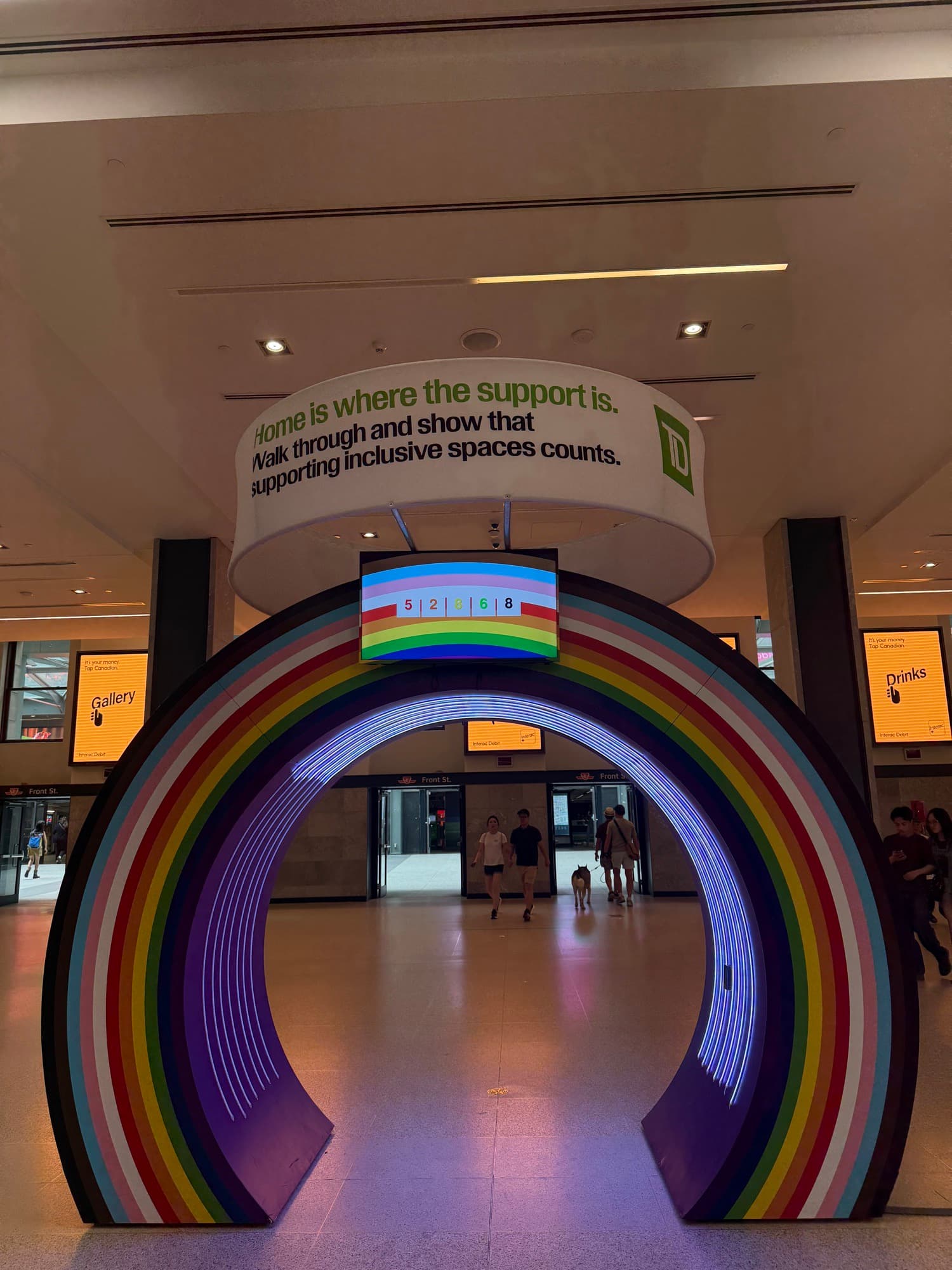 A giant rainbow letter C installation glowing inside a bank hall