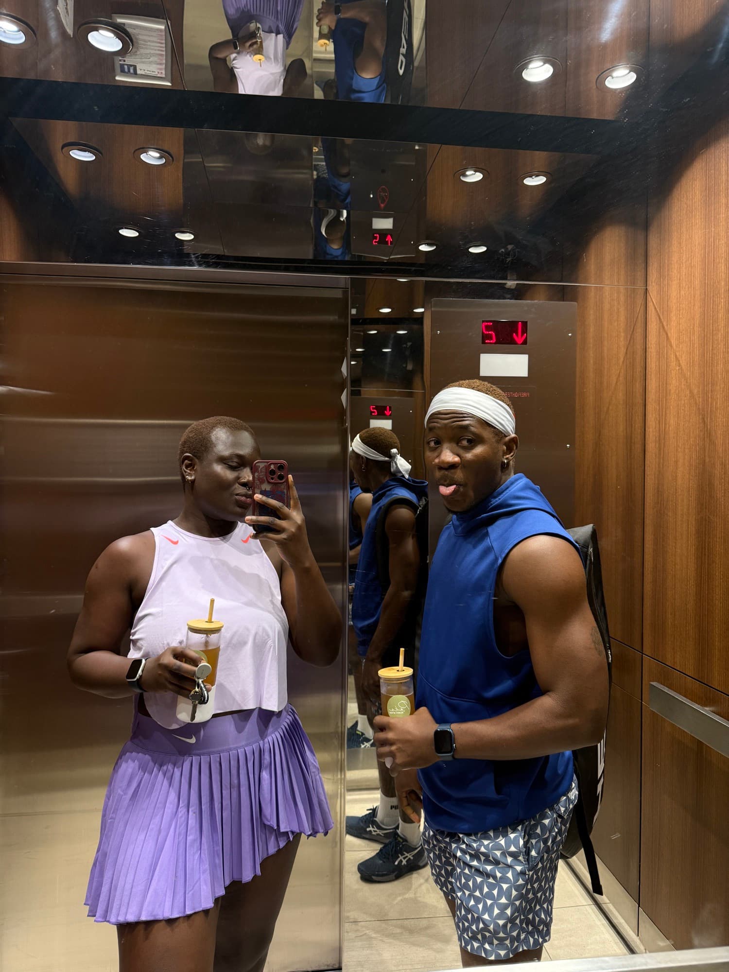 Elevator mirror selfie of a couple in tennis kit, drinks in hand