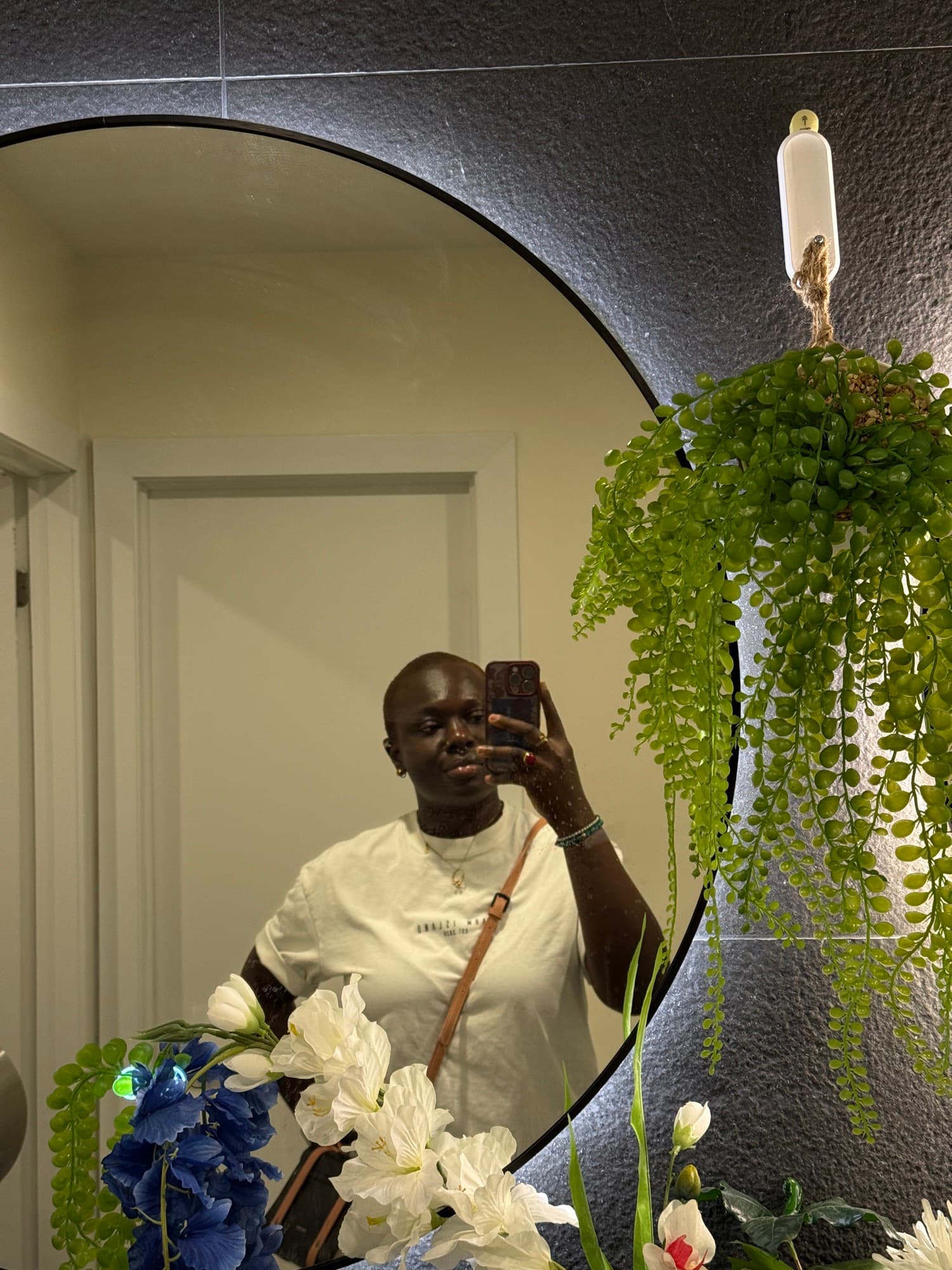 Mirror selfie of a woman in an oversized white tee, framed by a round mirror and trailing green plants