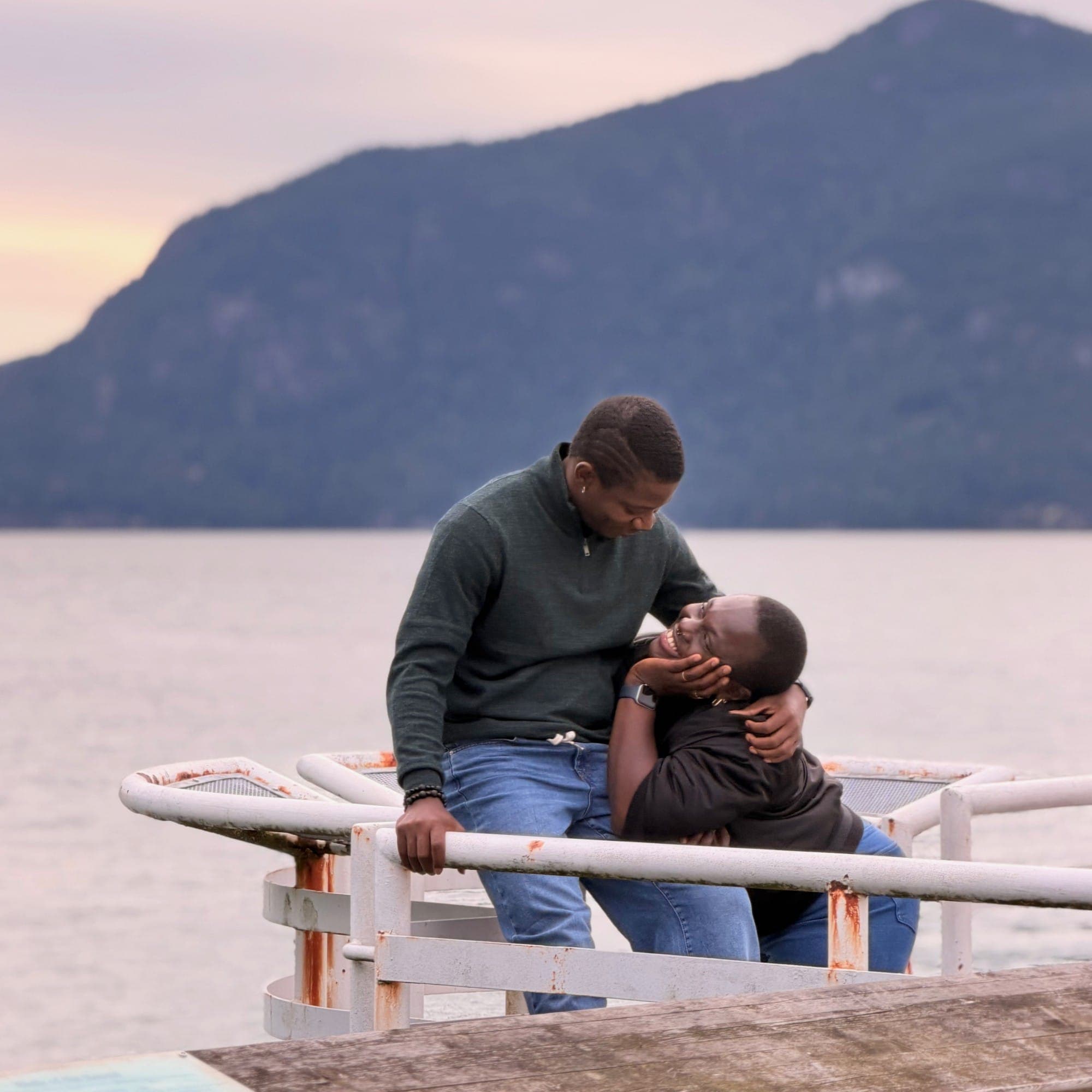 Sitting on a pier railing at dusk, holding her face as she laughs up at me
