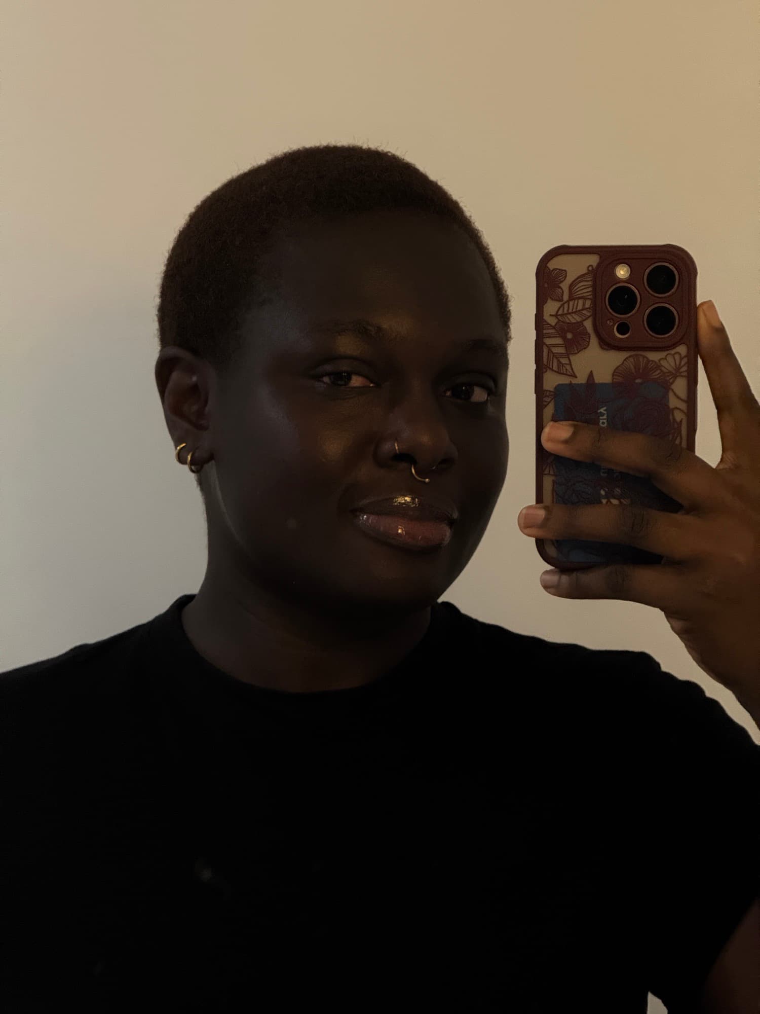 A close selfie of a woman with gold earrings and a septum ring in warm light