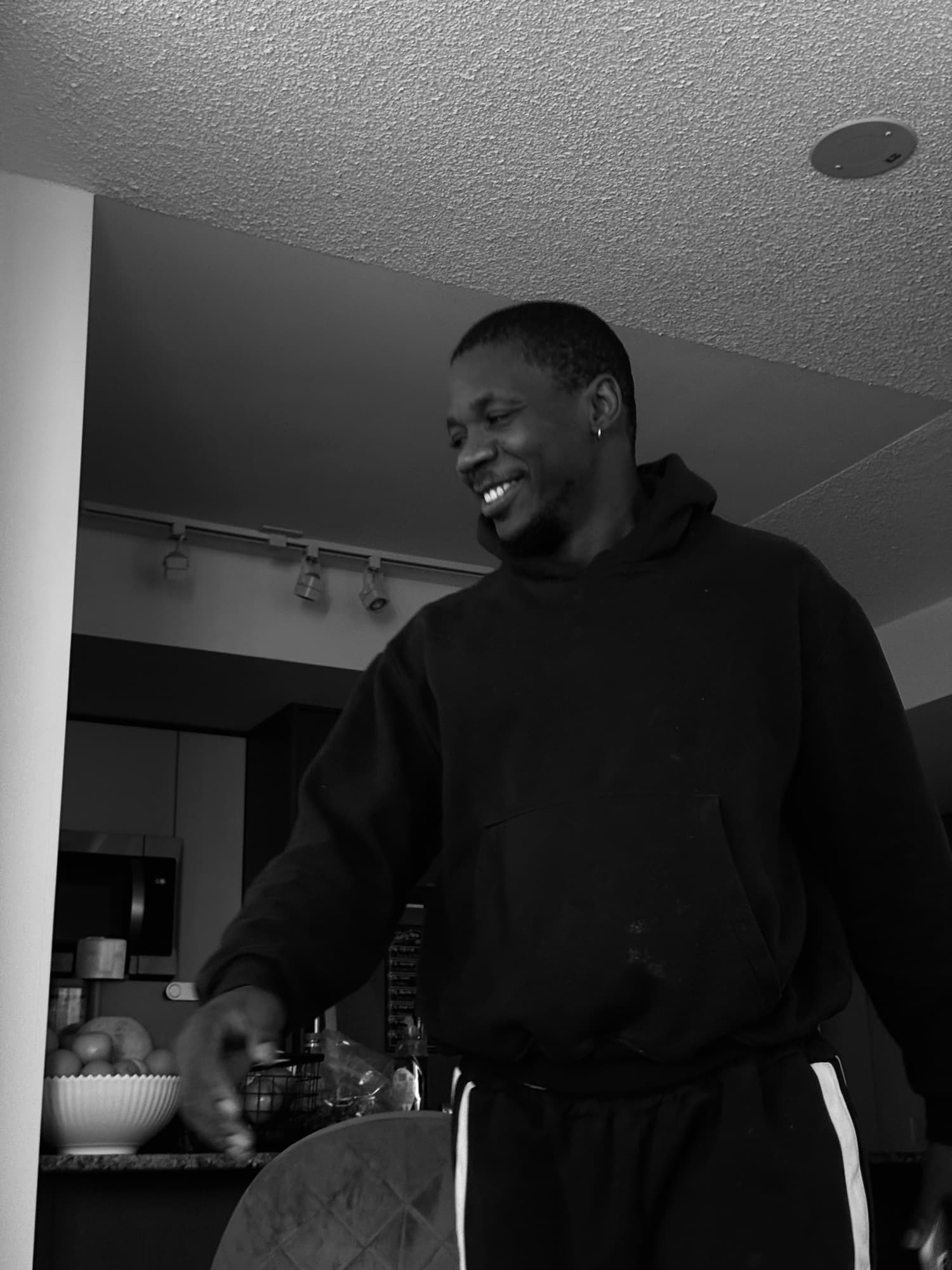 Black-and-white photo of a smiling man in a hoodie in a kitchen