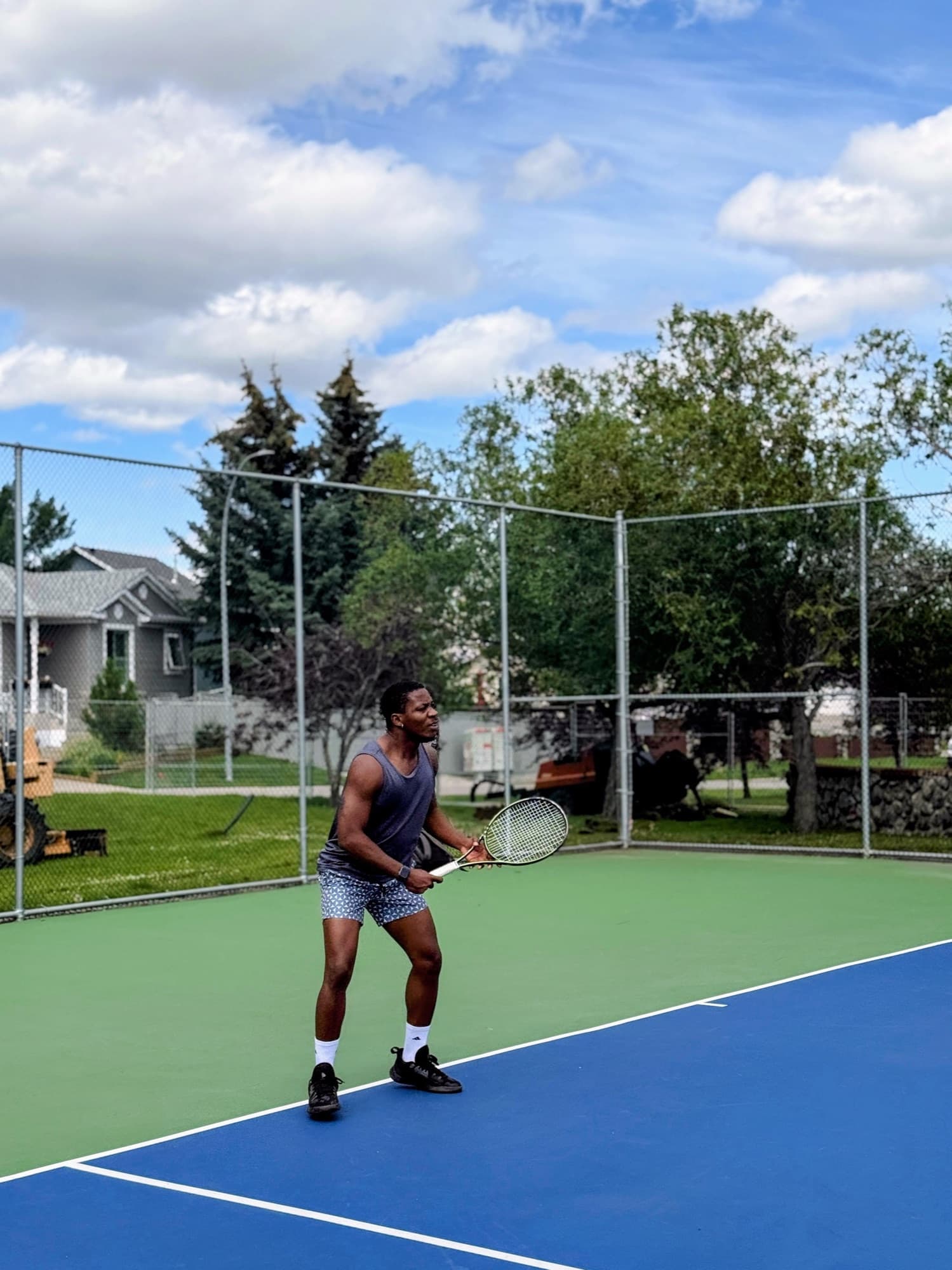 A tennis player in ready position on a blue court, racket up, watching the ball