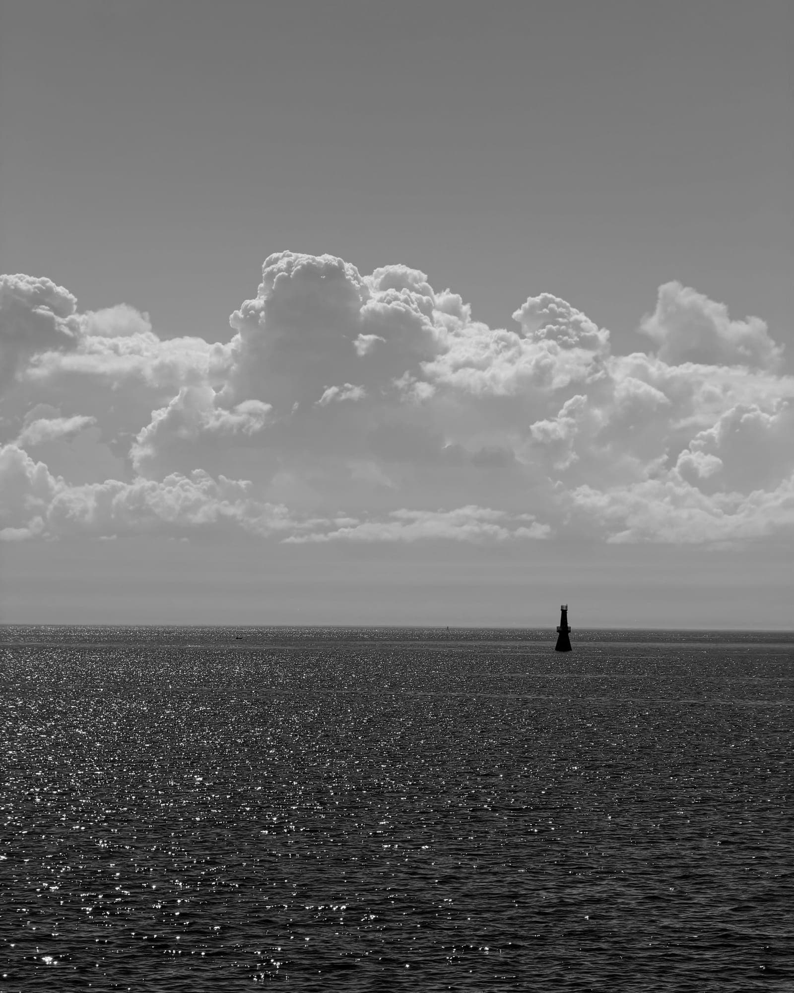 A single buoy on a glittering sea beneath a bank of cumulus, in black and white