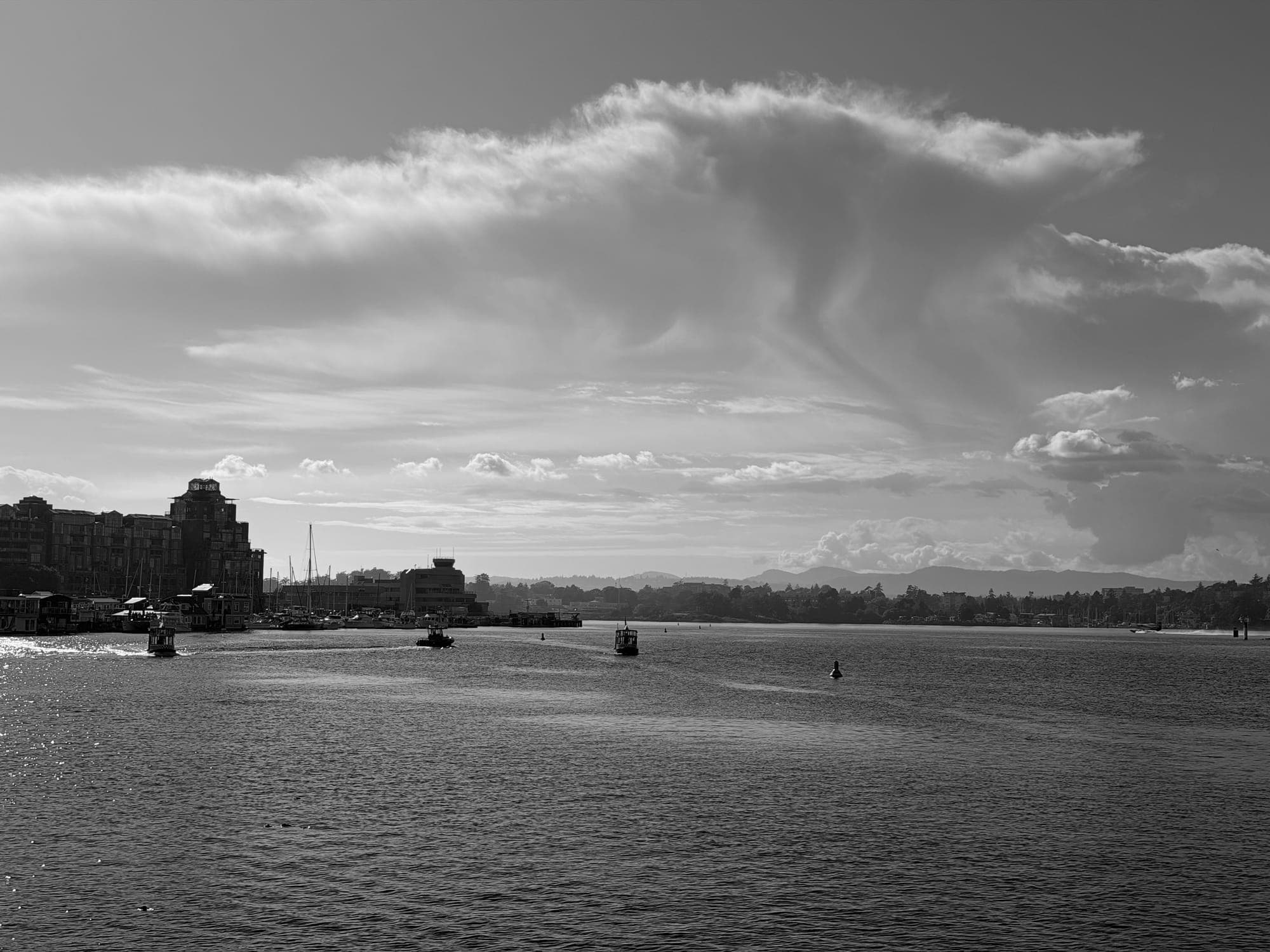 A sweep of cloud over the harbour with small boats on the water, in black and white