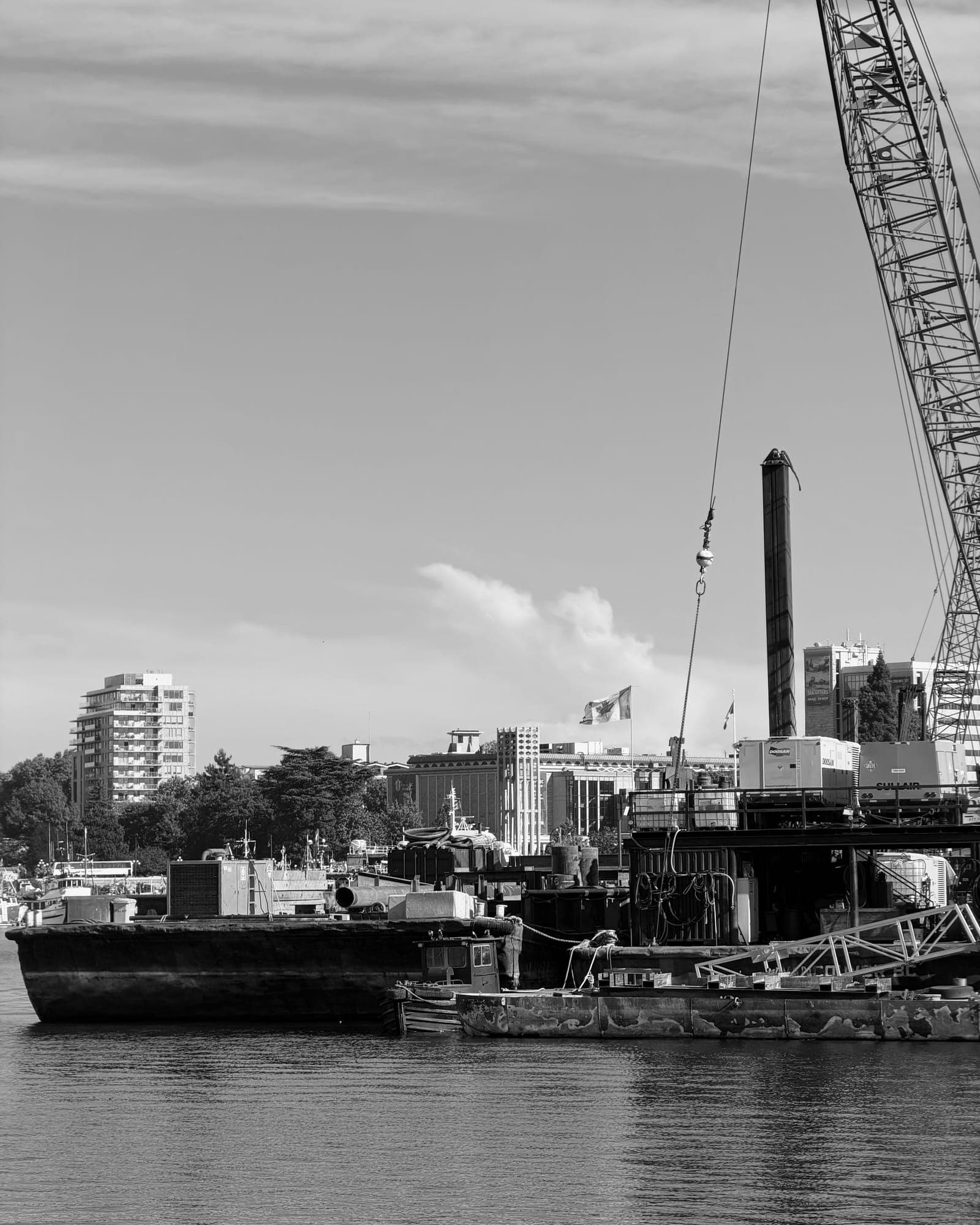 A construction crane and barge on the harbour, in black and white