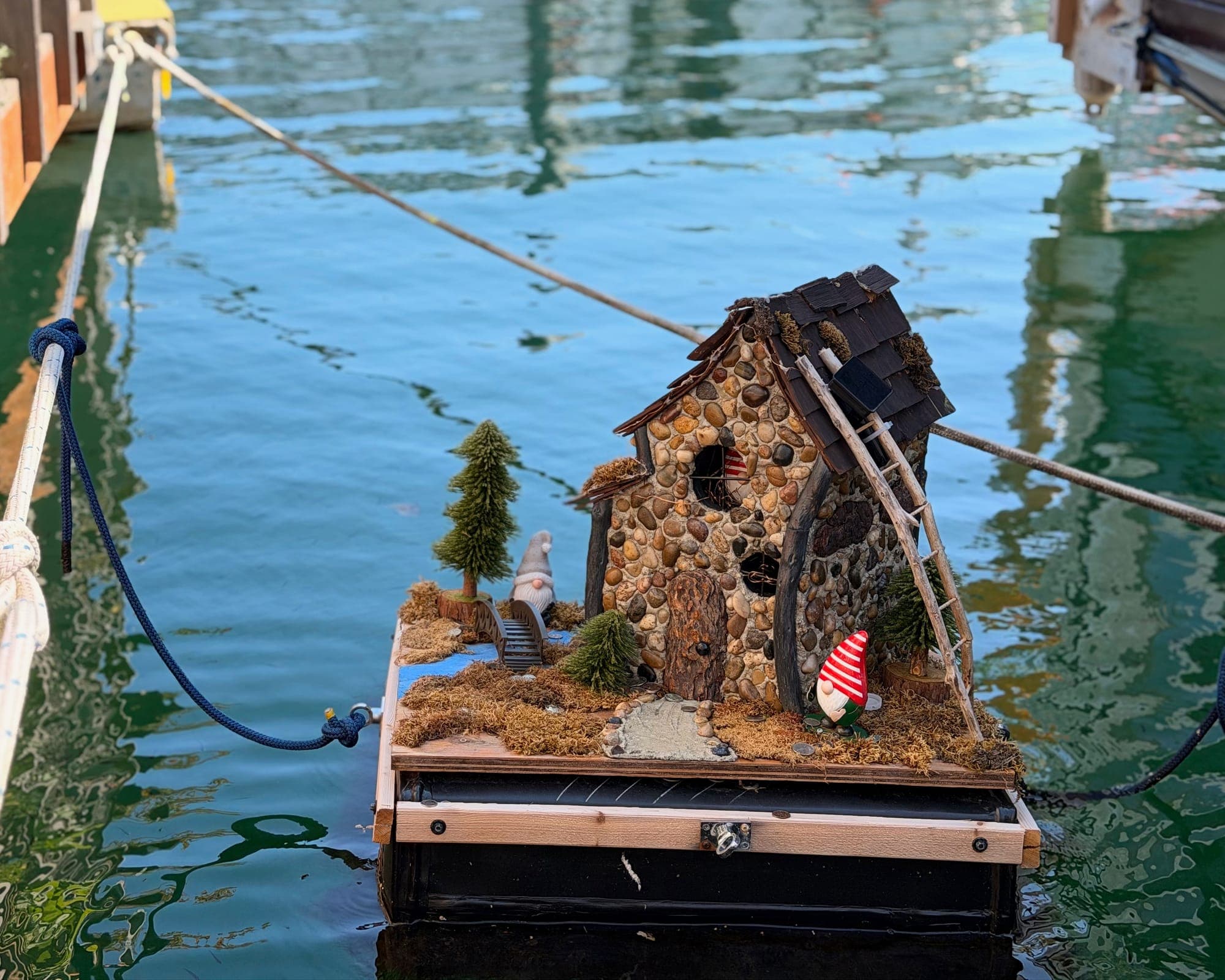 A miniature stone cottage floating on a raft in green harbour water