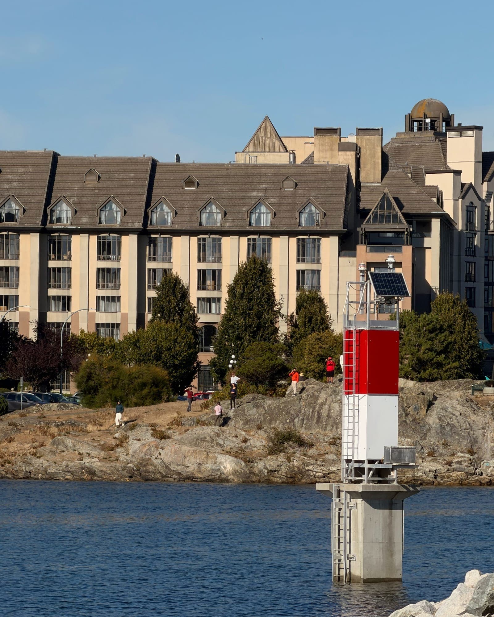 A red and white channel marker in front of a hotel on the waterfront