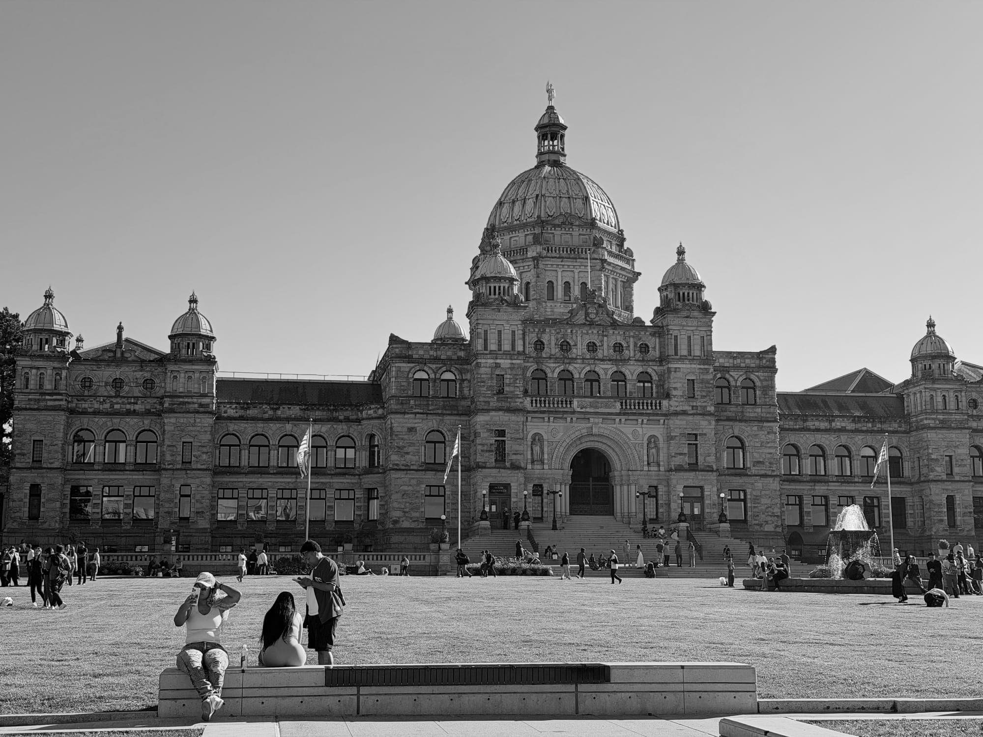 The British Columbia Parliament Buildings from across the lawn, a few people on the steps, in black and white