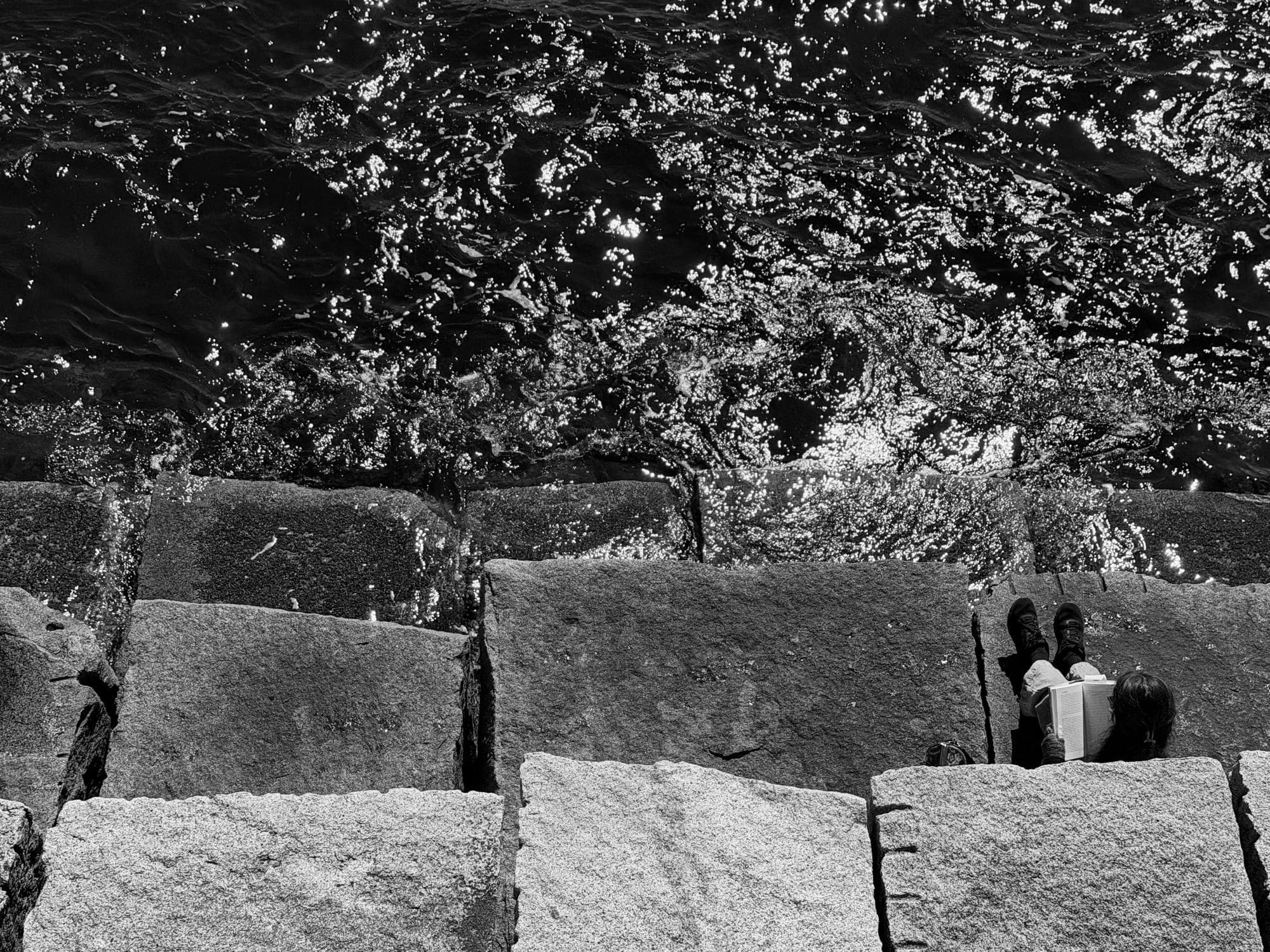 Granite blocks in hard light with tree shadows, a couple sitting at the corner of the frame, in black and white