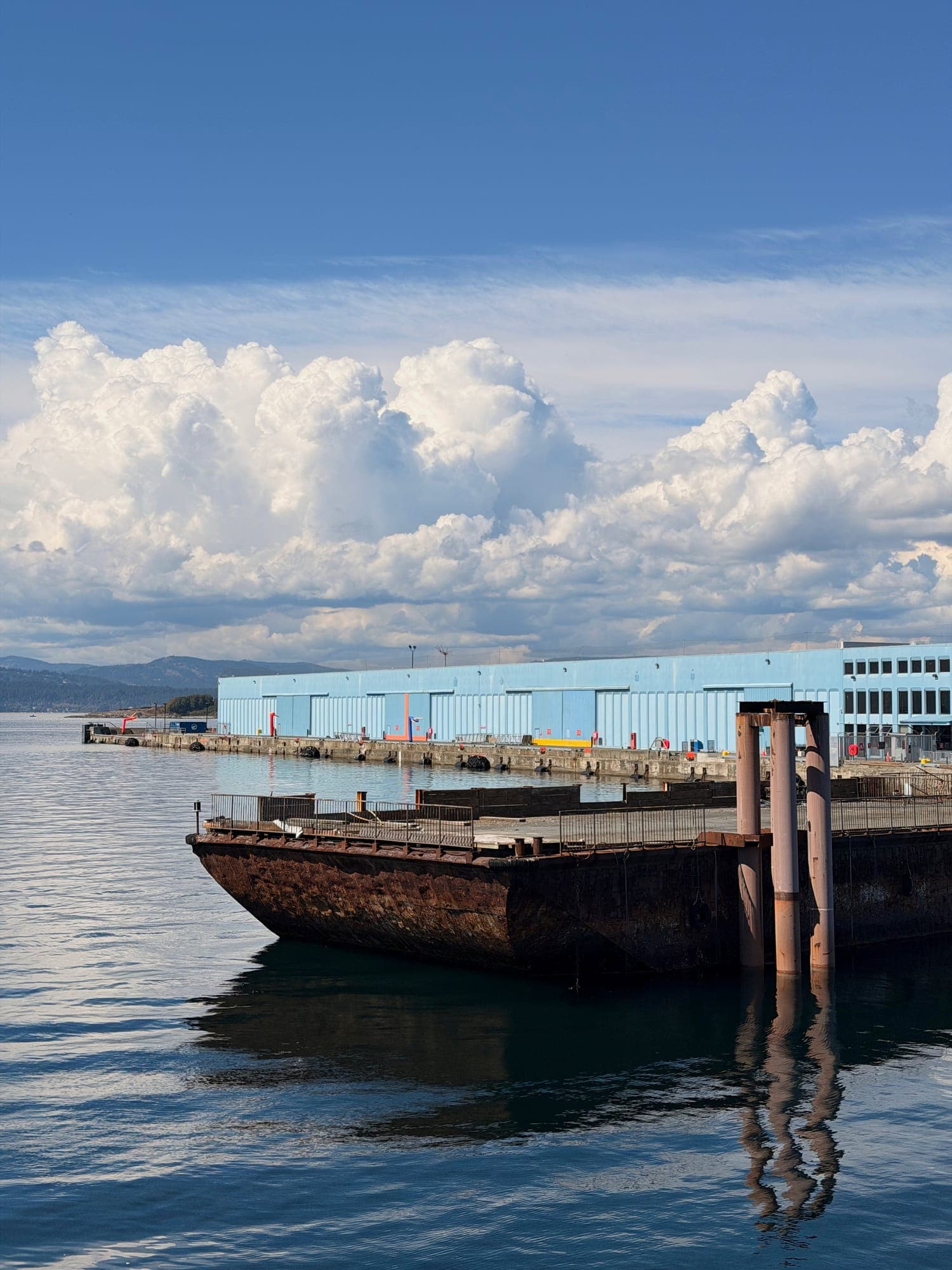 A rusted barge moored at a pier, clouds massing behind