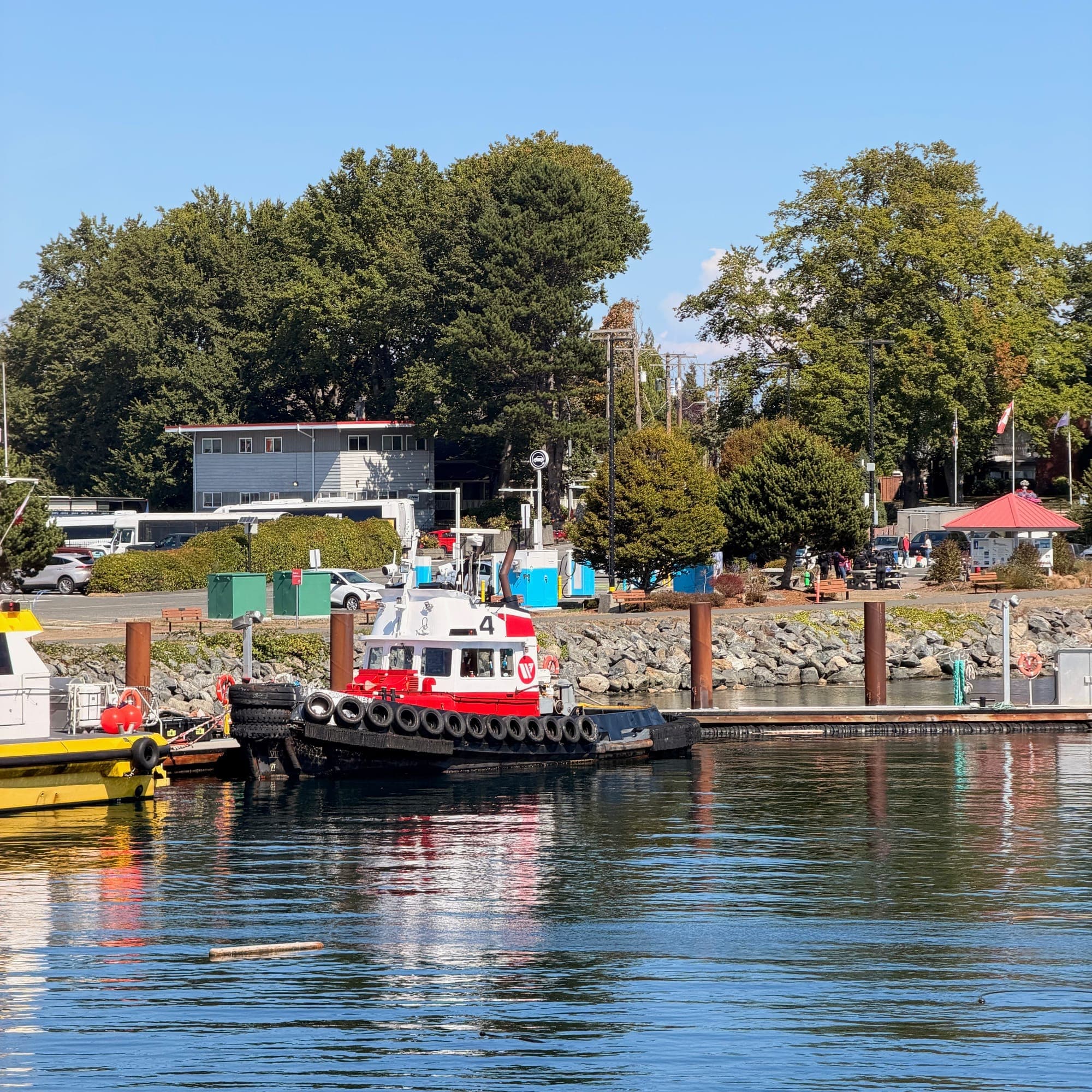A red tugboat moored beside float homes and green trees