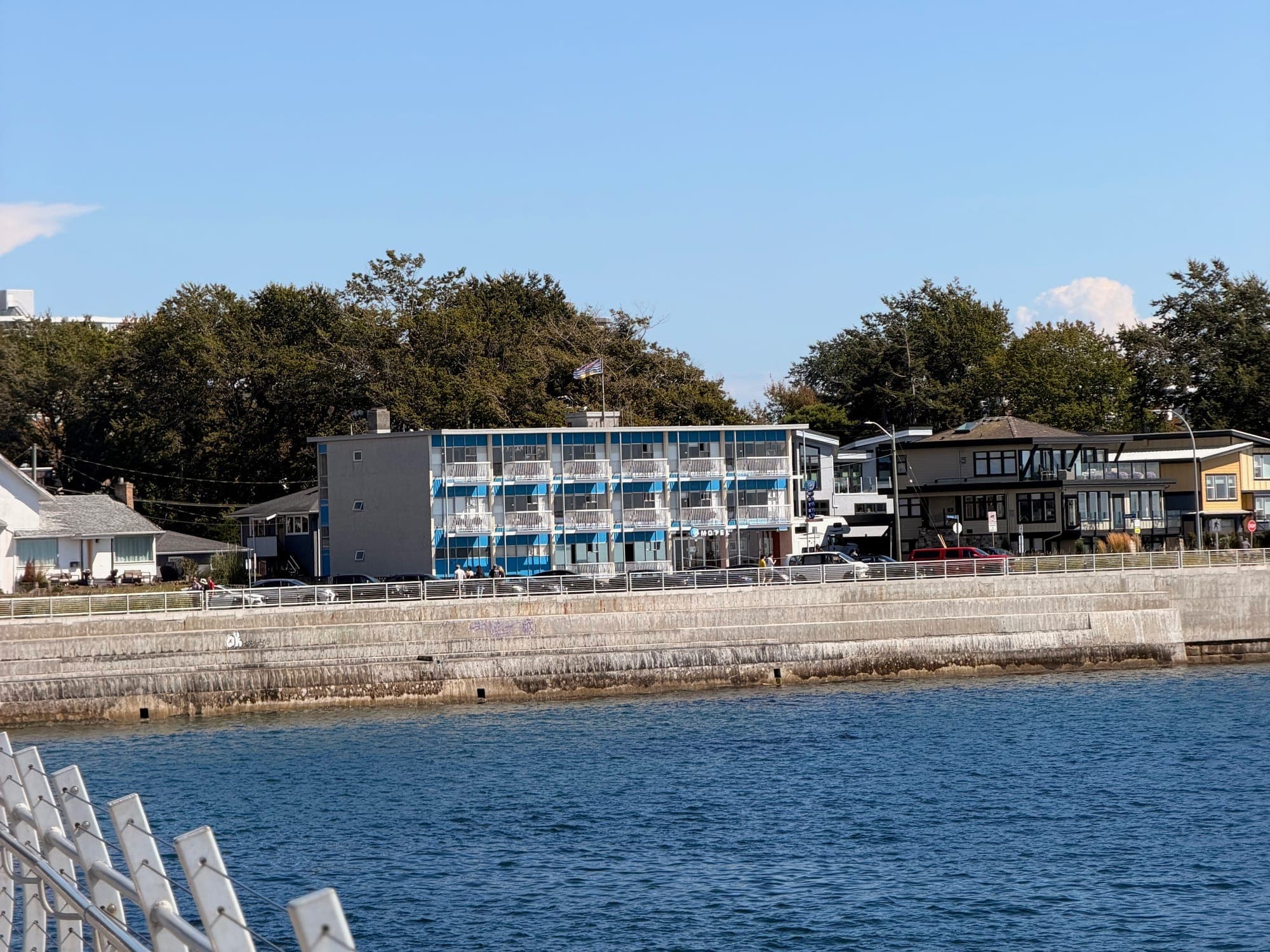 Low apartment blocks along a seawall, railings in the foreground