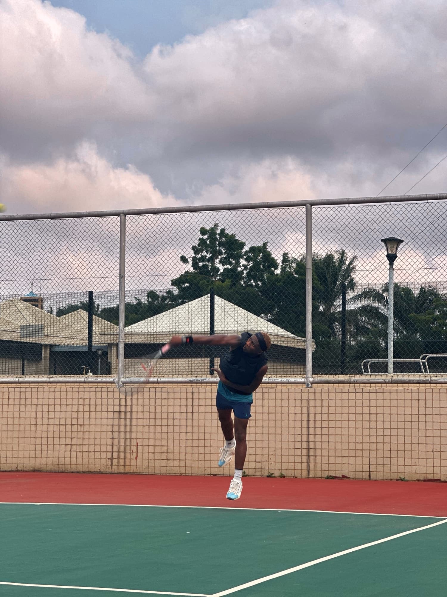Mid-serve on an outdoor court, ball tossed high, fully extended