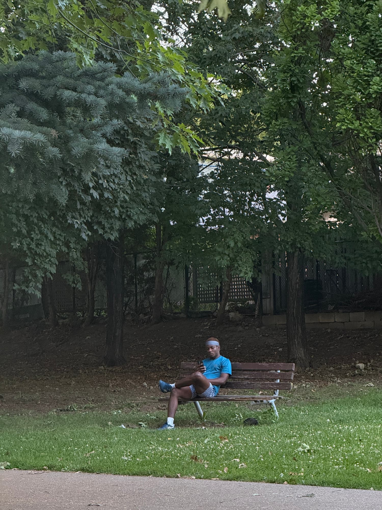 A tennis player sitting on a park bench beneath tall trees
