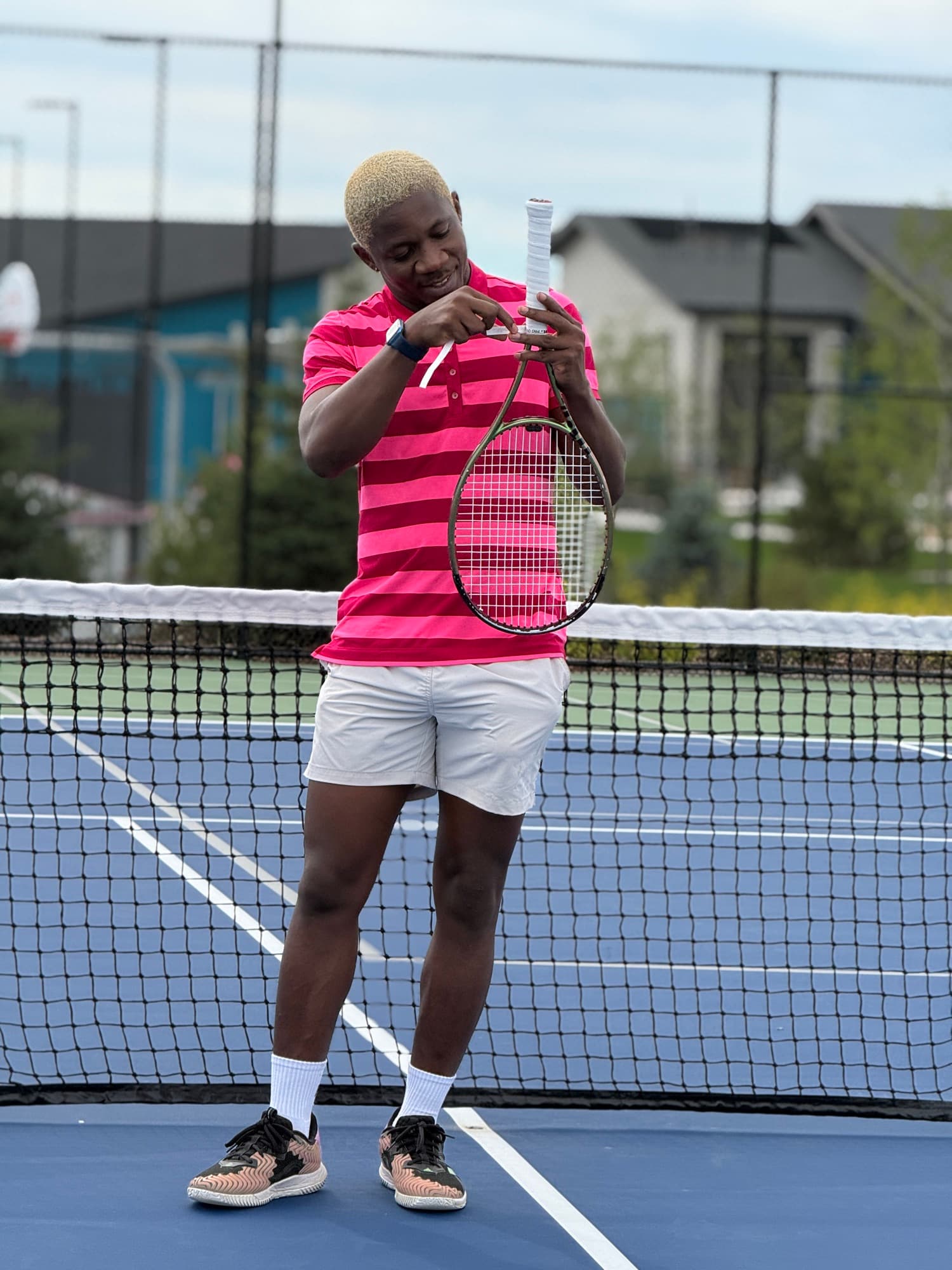 Re-wrapping a racket grip at the net in a pink striped polo