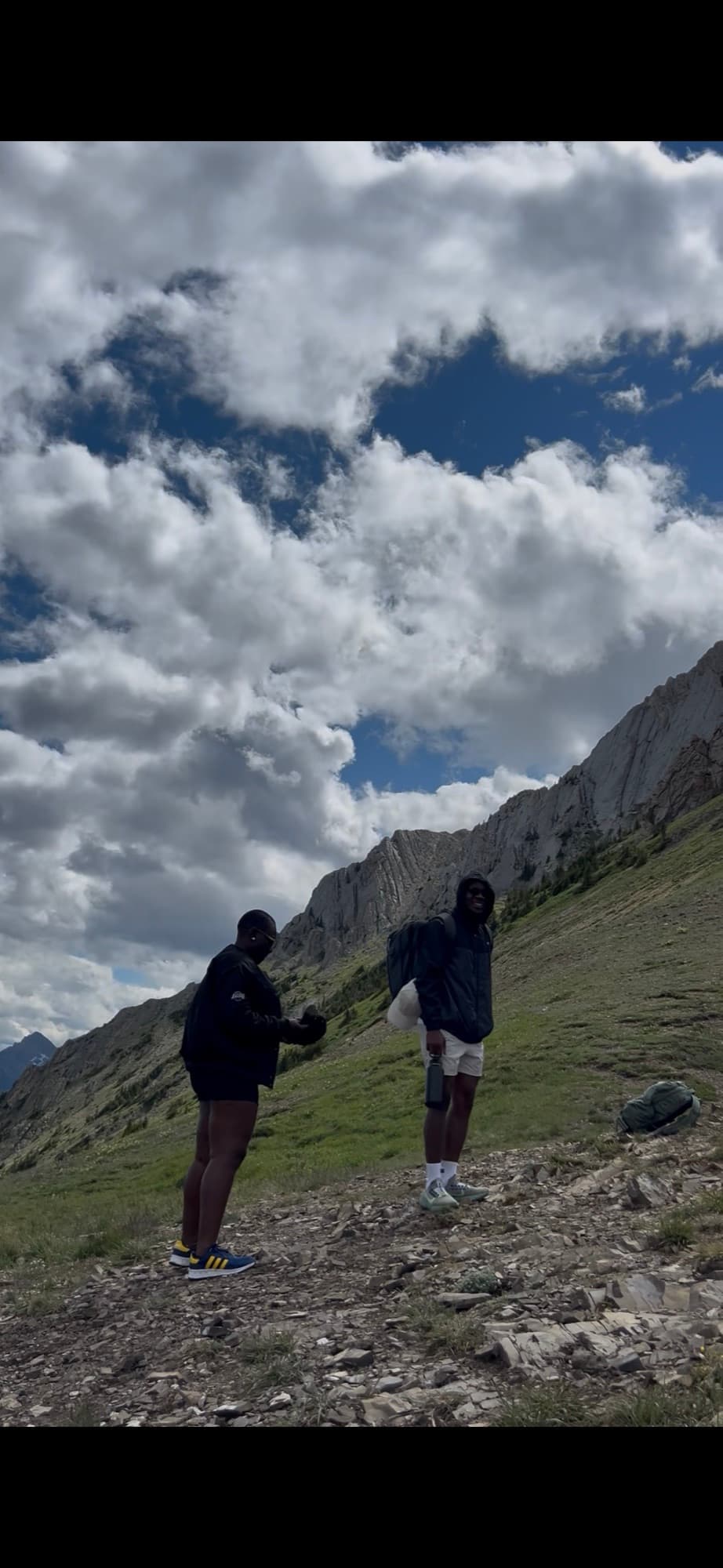 Two hikers pausing on a rocky alpine trail beneath a wall of cloud