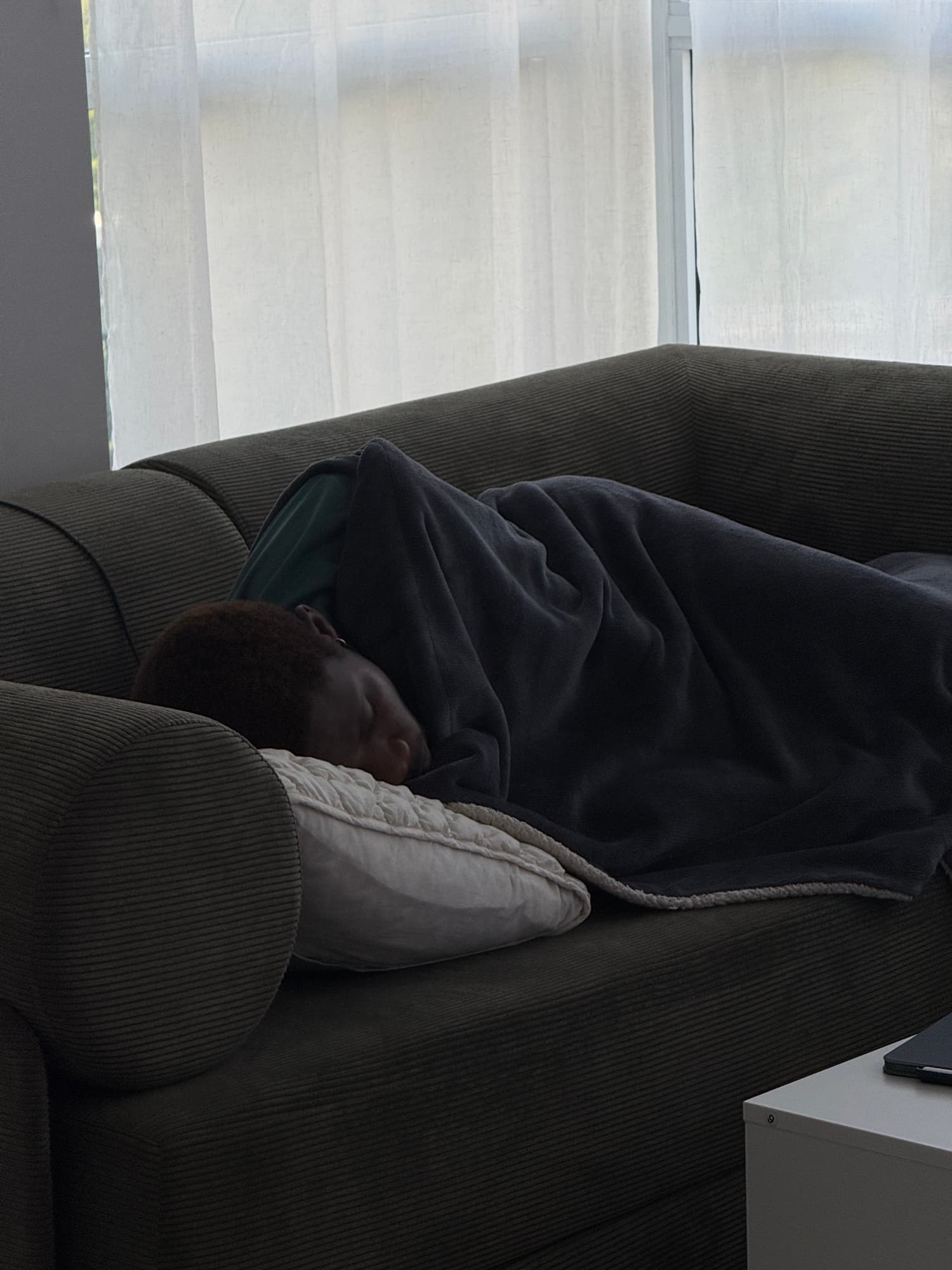 A person asleep beneath a dark blanket on a couch
